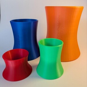 May include: A set of four concave cylindrical objects in red, blue, green, and orange. Each piece features a flared top and base with embossed text on the side. The red piece is labeled 'WIDE SMALL CHUCK', the blue 'WIDE MEDIUM CHUCK', and the orange 'WIDE XL CHUCK'.