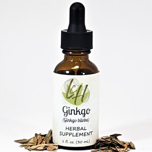 Puede incluir: Una botella de vidrio marrón con un cuentagotas negro, etiquetada como "Ginkgo (Ginkgo biloba) HERBAL SUPPLEMENT 30 ml." La botella está rodeada de hojas secas, lo que sugiere un producto herbal natural.