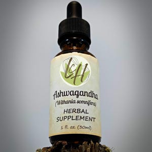 Op de afbeelding: Een bruine glazen fles met een zwarte druppeldop, met het label "Ashwagandha Herbal Supplement". Het etiket bevat de wetenschappelijke naam "Withania somnifera" en geeft de inhoud aan als 30 ml. De fles staat op een stuk hout.