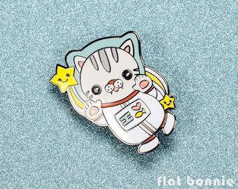 Può includere: Un gatto bianco che indossa una tuta da astronauta bianca con un cuore rosso e un pesce sul petto. Il gatto tiene una stella gialla con un viso sorridente. Il gatto è circondato da un arcobaleno blu e giallo.