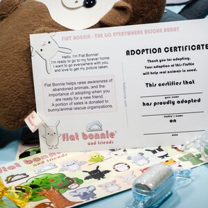 May include: Adoption certificate for a Flat Bonnie plush toy. The certificate is printed on white cardstock with black text. The certificate states that the adopter has proudly adopted the Flat Bonnie. The certificate is next to a Flat Bonnie plush toy and stickers.