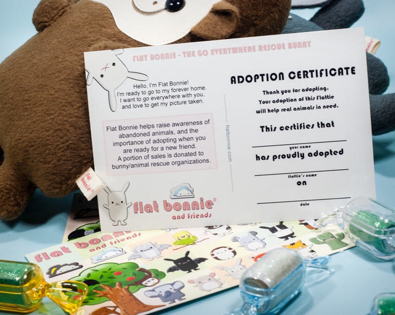 May include: Adoption certificate for a Flat Bonnie plush toy. The certificate is printed on white cardstock with black text. The certificate states that the adopter has proudly adopted the Flat Bonnie. The certificate is next to a Flat Bonnie plush toy and stickers.