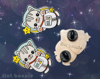 Puede incluir: Dos pines de esmalte con un gato de dibujos animados que lleva un traje de astronauta. El gato flota en el espacio con estrellas y una estrella fugaz. La parte posterior del pin muestra el texto "flat bonnie".