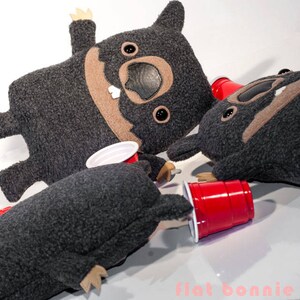 May include: Three gray plush toys shaped like dogs with brown accents and black eyes. The toys are holding red plastic cups.
