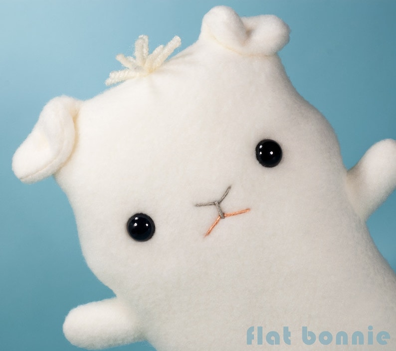 May include: White plush toy shaped like a bunny with black eyes and a stitched nose. The toy has a fluffy white tail and is made of soft fabric.