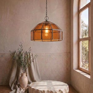 May include: A pendant light fixture featuring a hexagonal amber-colored glass shade with a dark metal frame, suspended by a matching metal chain. The lamp emits a warm glow from a single light bulb visible through the textured glass panels.