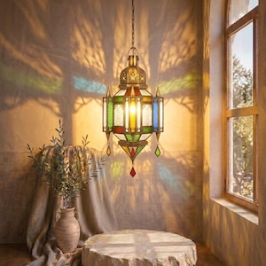 May include: A hanging metal lantern featuring stained glass panels in red, green, yellow, and blue. The lantern has an intricate brass-toned frame with pointed accents and small dangling glass charms, suspended from the ceiling by a metal chain.