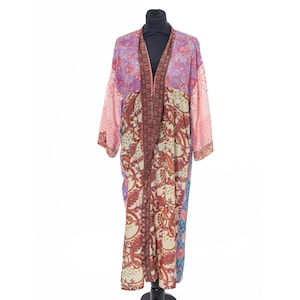 May include: A long, open-front kimono robe with a patchwork design. The robe features a mix of floral and paisley patterns in shades of pink, purple, cream, and red. The sleeves are long and the robe is displayed on a black mannequin.