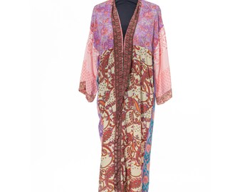 May include: A long, open-front kimono robe with a patchwork design. The robe features a mix of floral and paisley patterns in shades of pink, purple, cream, and red. The sleeves are long and the robe is displayed on a black mannequin.