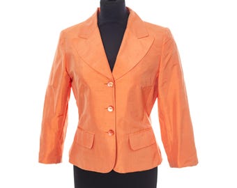 May include: An orange blazer with three buttons and two front pockets. The blazer is displayed on a black mannequin. The sleeves are three-quarter length, and the fabric has a subtle sheen. The blazer is a classic style.