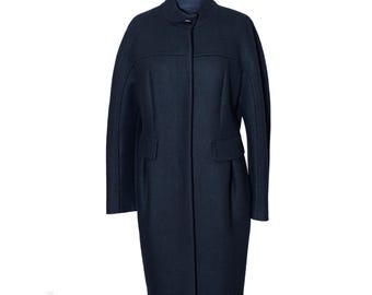 May include: A dark navy blue coat featuring a high stand-up collar, long sleeves, and a concealed front button closure. The coat has a structured silhouette with horizontal seam detailing across the chest and two flap pockets at the waist.