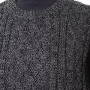 May include: A close-up of a charcoal gray cable-knit sweater. The sweater features a crew neck and a textured pattern of vertical and diamond-shaped cable designs. The knitwear is displayed on a mannequin.