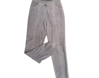 May include: A pair of gray suede pants. The pants have a button and zipper closure, two front pockets, and belt loops. The pants are a neutral color and appear to be vintage.