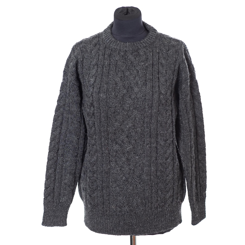 May include: A gray cable-knit sweater with a crew neck. The sweater is displayed on a mannequin and features a textured pattern across the front and sleeves. The sleeves are long and the overall style is classic.