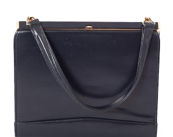 May include: A navy blue handbag with a rectangular shape and a gold-colored clasp. The bag has a single handle and a smooth, glossy finish. The bag's design is simple and elegant, suitable for various occasions.