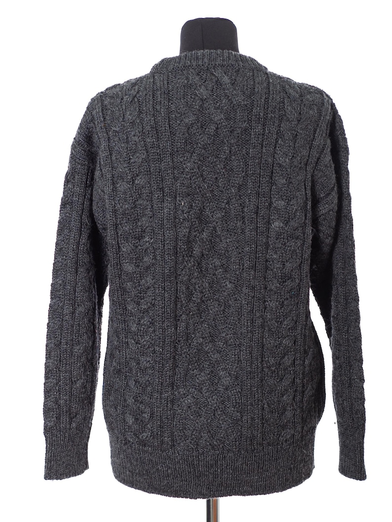 May include: A dark gray cable-knit sweater with a crew neck. The back of the sweater is displayed, showcasing the intricate knit pattern. The sleeves are long, and the sweater appears to be made of a thick, warm material.