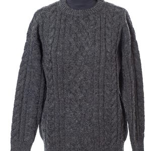May include: A gray cable-knit sweater displayed on a mannequin. The sweater features a crew neck and a textured pattern. The color is a medium gray, and the knit appears thick and warm, suitable for colder weather. The sleeves are long, and the overall style is classic.