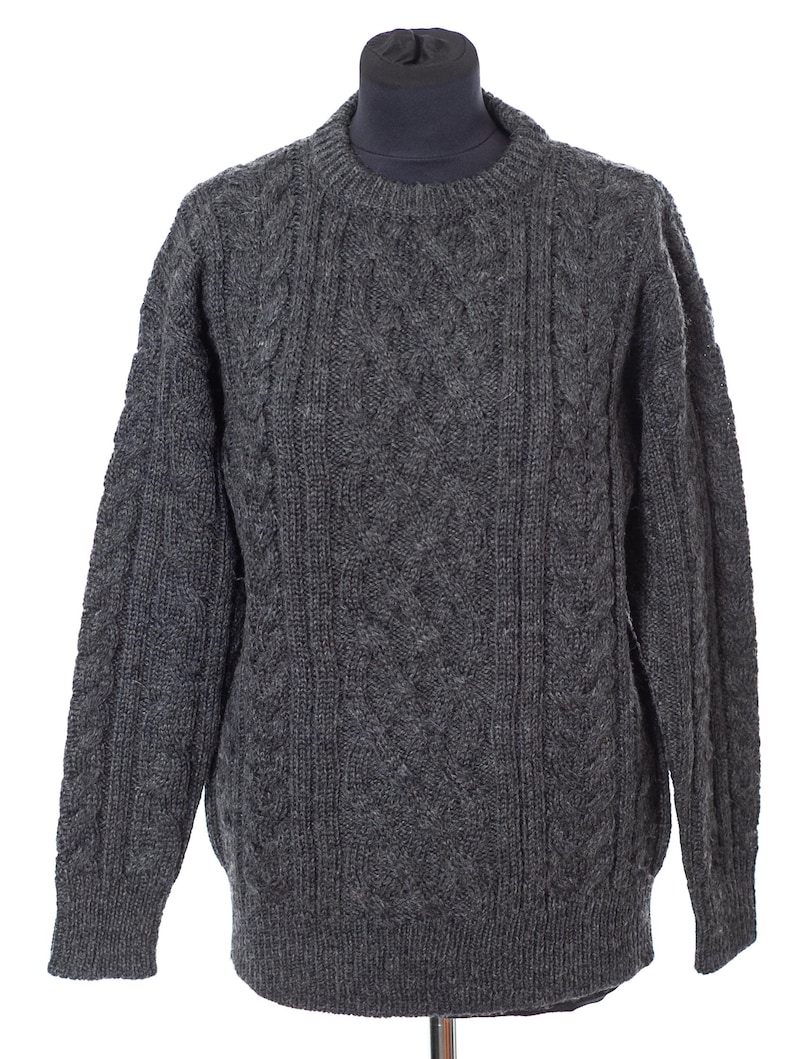 May include: A gray cable-knit sweater displayed on a mannequin. The sweater features a crew neck and a textured pattern. The color is a medium gray, and the knit appears thick and warm, suitable for colder weather. The sleeves are long, and the overall style is classic.