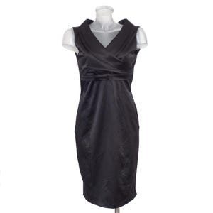 May include: A sleeveless black dress featuring a V-neckline with wide lapel-style collar detailing, a fitted bodice with a horizontal band at the waist, and a knee-length skirt. The garment is constructed from a smooth, solid black fabric.