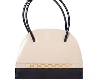 May include: A cream-colored handbag with a black bottom and black handles. The bag features a gold chain design across the front. The handles are curved and attached to the top of the bag. The bag is a half-circle shape.