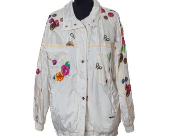May include: An off-white windbreaker jacket featuring a colorful print of various flowers and small circular motifs. The jacket has a high collar, a front snap-button closure, two chest pockets, long sleeves with elastic cuffs, and the word HEAD printed.