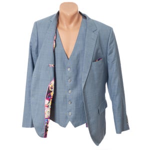 Peut inclure: Un costume trois pièces bleu clair présenté sur un mannequin. Le costume comprend une veste, un gilet et un pantalon. La veste a un motif à carreaux et une pochette. Le gilet a des boutons. La doublure intérieure de la veste présente une impression graphique colorée.