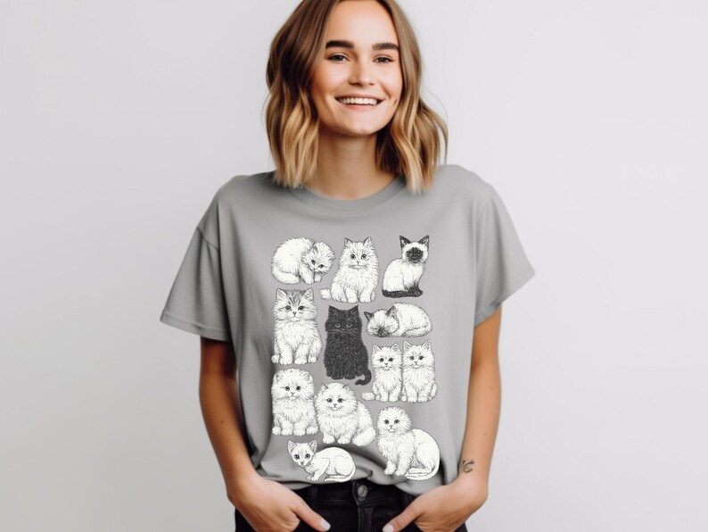 May include: A gray t-shirt featuring a collection of illustrated cats in various poses. The cats are depicted in black and white, with one solid black cat. The shirt is a casual style, suitable for cat lovers.