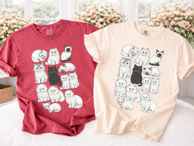 May include: Two short-sleeved t-shirts, one red and one cream, each featuring a repeating pattern of illustrated cats in various poses. The cats are in black and white, with some in a sitting or sleeping position.