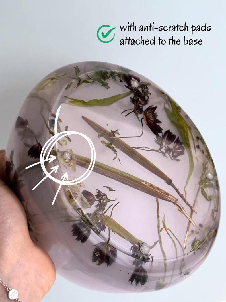 May include: A round, translucent, light purple resin bowl embedded with dried dark purple flowers and green stems. The base features small, clear anti-scratch pads, as indicated by the text "with anti-scratch pads attached to the base."