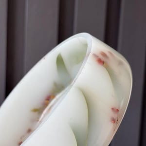 May include: A translucent white resin bangle bracelet featuring embedded dried green leaves and small pink flower buds. The circular accessory has a smooth, polished finish and a rounded profile, showcasing the delicate botanical elements suspended within.