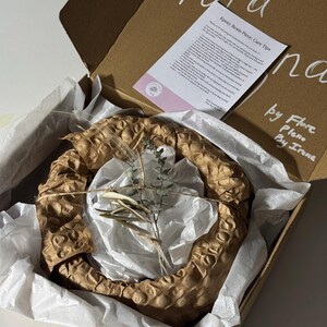 May include: A brown cardboard shipping box containing a circular object wrapped in brown honeycomb paper and white tissue paper. A small sprig of dried eucalyptus is tied to the top with twine. A care instruction card is included inside the box.