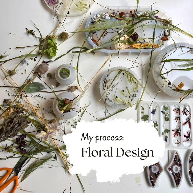 May include: A collection of silicone molds filled with dried flowers, grasses, and botanical elements, alongside orange-handled scissors. A white overlay features the black text: My process: Floral Design, showcasing the craft of resin art.