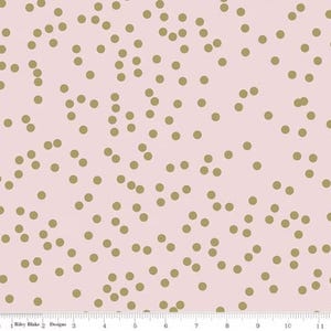 May include: Pink fabric with a pattern of scattered gold-colored dots. The dots are of varying sizes and are evenly distributed across the surface. The fabric has a soft, pastel color palette.