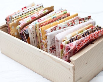 May include: A wooden crate filled with colorful fabric scraps. The fabric is arranged in a neat stack and includes various patterns and colors, including floral, polka dot, and geometric designs. The crate is made of light wood and has a natural finish.