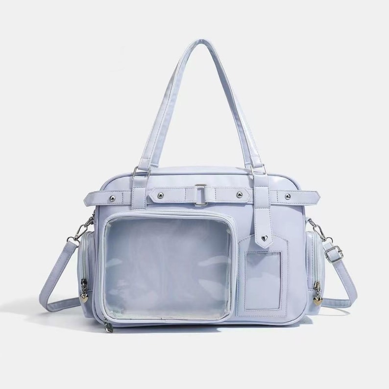 May include: A light blue handbag with a clear front pocket and a shoulder strap. The bag has a rectangular shape with a top handle and side pockets. It features silver-colored hardware and a buckle closure.