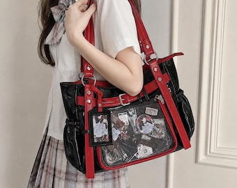 May include: A black tote bag with red trim and straps, featuring a clear front pocket filled with various anime-style character cards and circular pins. The bag includes a matching black and red luggage-style tag hanging from a silver ring.