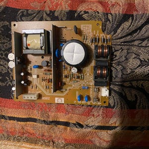 Peut inclure: Une carte de circuit imprimé de couleur beige avec divers composants électroniques, dont un transformateur, des condensateurs et des résistances. La carte comporte des éléments bleus, noirs et bruns. Le texte comprend "CAUTION" et "PF-LPS 1-468-604-41".