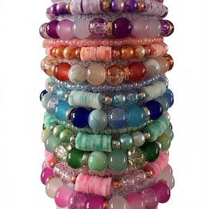 May include: A collection of colourful beaded bracelets in shades of pink, purple, green, blue, and orange. The bracelets feature various bead sizes and shapes, including round, disc, and irregular beads. Some bracelets have metallic accents.