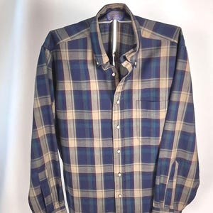 May include: A long-sleeved plaid shirt in navy blue, teal, and tan. The button-down shirt features a button-down collar, a chest pocket, and buttoned cuffs. The shirt is displayed on a hanger against a white background.
