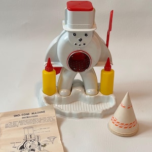 Può includere: Una macchina Sno-Cone vintage a forma di pupazzo di neve, con cappello a cilindro e bocca rossi. Include due bottiglie gialle e un cono di carta. È incluso anche un foglio di istruzioni.