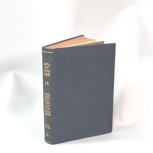 Puede incluir: Un libro antiguo con una cubierta azul oscuro, titulado "Models New Electric Library IV". El lomo del libro muestra texto adicional sobre los principios de la corriente alterna y el factor de potencia. Las p&aacute;ginas est&aacute;n envejecidas y el libro est&aacute; sobre un fondo blanco.