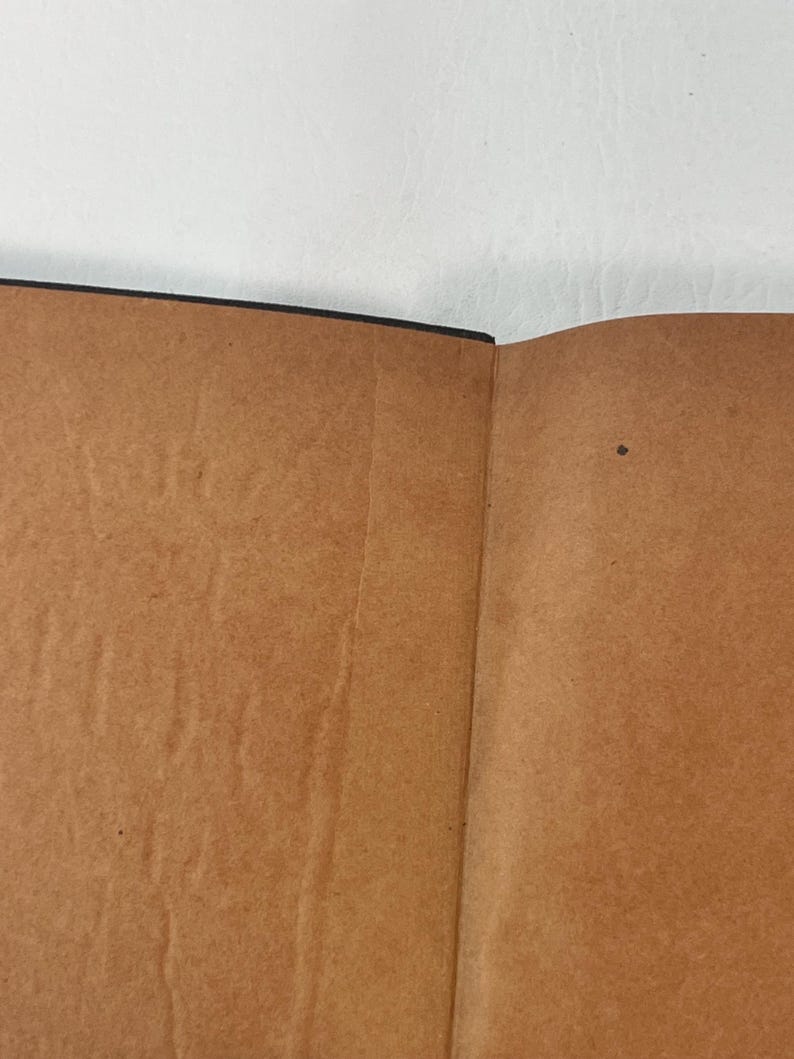Puede incluir: Libro abierto con p&aacute;ginas marrones y lomo negro. Las p&aacute;ginas tienen un aspecto texturizado con pliegues y ligera decoloraci&oacute;n. El libro est&aacute; abierto, revelando las p&aacute;ginas interiores sobre un fondo blanco.