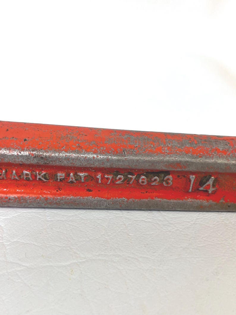 May include: Close-up of a weathered, red metal tool. The tool has the text "MARK PAT 1727623 14" embossed on its surface. The metal shows signs of age and wear.