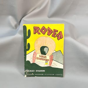 Puede incluir: Un programa de recuerdo vintage para el Campeonato Mundial de Rodeo del Estadio de Chicago. La portada presenta la palabra "RODEO" en letras rojas, una carreta cubierta y un cactus sobre un fondo amarillo. El programa es verde en la parte inferior.