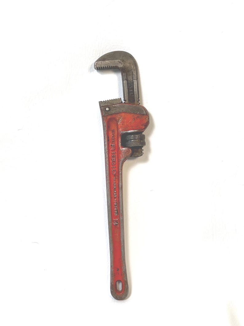 May include: A vintage red and gray pipe wrench, a hand tool with adjustable jaws. The wrench is marked with the number 14, indicating its size in inches. The tool is designed for gripping and turning pipes.