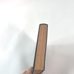Puede incluir: Un libro antiguo con una cubierta de cuero marr&oacute;n oscuro y p&aacute;ginas envejecidas de color beige. El lomo del libro es visible, mostrando el desgaste del tiempo. Las p&aacute;ginas est&aacute;n ligeramente amarillentas, lo que indica la edad.