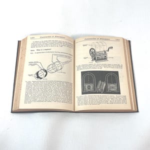 Puede incluir: Un libro abierto con cubiertas negras, que muestra diagramas y texto sobre la construcci&oacute;n de alternadores. Las p&aacute;ginas est&aacute;n amarillentas, con t&eacute;rminos t&eacute;cnicos e ilustraciones de componentes mec&aacute;nicos.