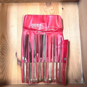 May include: A set of American Swiss files in a red vinyl case. The case is labeled "SIMONDS SAW AND STEEL" and "American Swiss". The files are various shapes and sizes, with metal handles. The set is displayed in a wooden box.