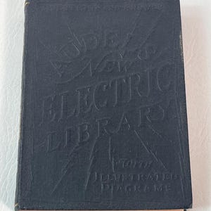 Puede incluir: Un libro vintage azul oscuro titulado "Audel's Electric Library" con letras e ilustraciones en relieve. La portada del libro tambi&eacute;n presenta el texto "Illustrated Diagrams". El libro tiene bordes dorados.