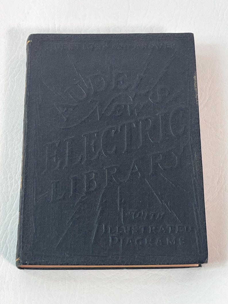 Puede incluir: Un libro vintage azul oscuro titulado "Audel's Electric Library" con letras e ilustraciones en relieve. La portada del libro tambi&eacute;n presenta el texto "Illustrated Diagrams". El libro tiene bordes dorados.